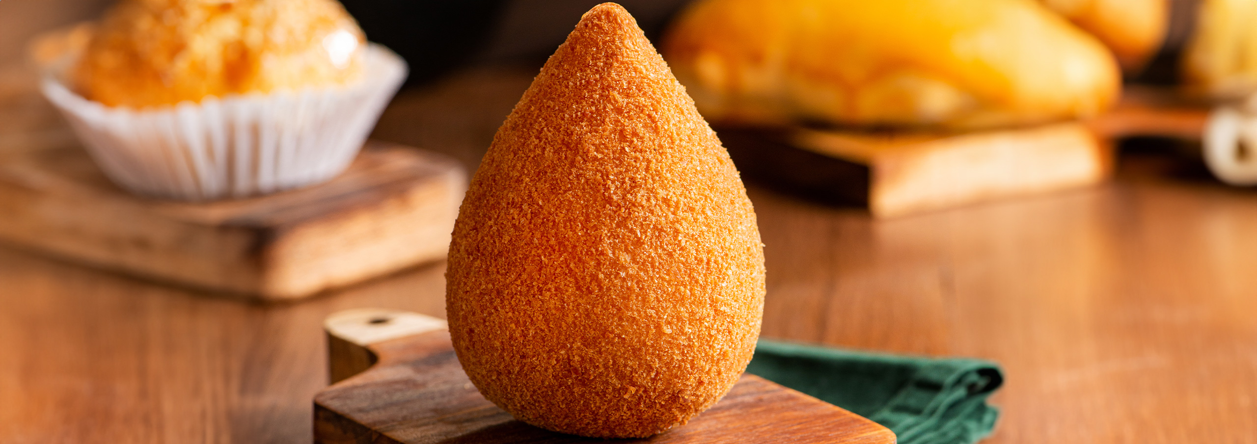 Coxinha dourada em destaque com salgados ao fundo